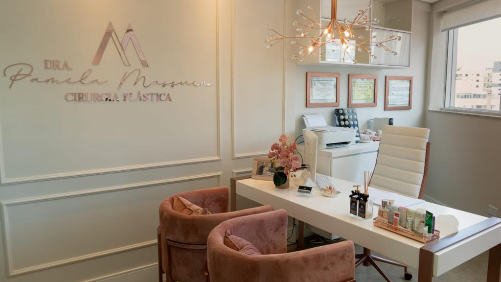 Sala de consulta com o nome da Dra. Pamela Massuia na parede, poltronas rosadas e lustre de cobre
