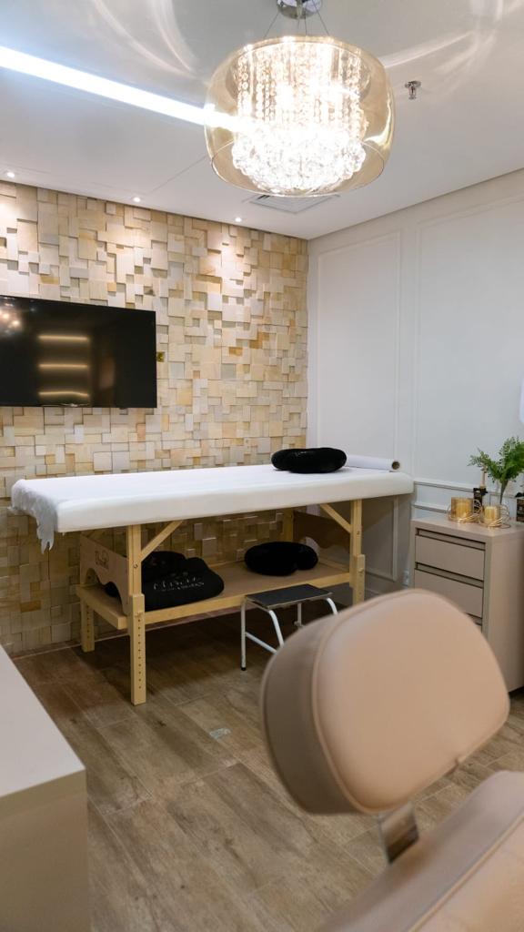 Sala de procedimentos com maca, parede de pedra clara e lustre de cristal