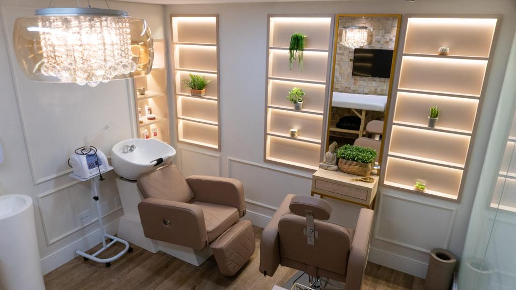 Sala de estética com poltronas reclináveis, lavatório e nichos iluminados com plantas